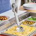 A person in gloves holding a Vollrath Jacob's Pride slotted stainless spoon over food on a plate.