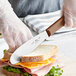 A person using a Choice stainless steel sandwich spreader to cut a sandwich.