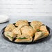 A WNA Comet black round catering tray with sandwiches on a table.