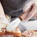 A person using a Choice stainless steel scalloped sandwich spreader to cut a sandwich.