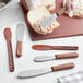A Choice stainless steel sandwich spreader with a brown handle being used to spread food on a piece of bread.