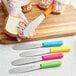 A person using a Choice stainless steel sandwich spreader with a neon pink handle to spread food on a piece of bread.