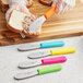 A Choice stainless steel sandwich spreader with a neon orange handle spreading spread on a sandwich.