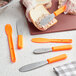 A person using a Choice sandwich spreader with a neon orange handle to spread food on a piece of bread.