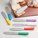 A person using a Choice stainless steel sandwich spreader with a purple handle to spread food on a piece of bread.