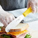 A person slicing a sandwich with a Choice stainless steel sandwich spreader.