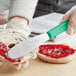 A person spreading jam on a bagel with a Choice stainless steel sandwich spreader with a green handle.