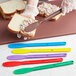 A hand in a glove spreads spread on a sandwich with a red Choice sandwich spreader.