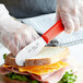 a person's hands in gloves cutting a sandwich with a knife