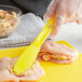 A person's hand with a Choice yellow polypropylene sandwich spreader over chicken breasts.