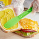 A person spreading mustard on a sandwich with a Choice neon green polypropylene sandwich spreader.