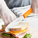 A person using a Choice scalloped sandwich spreader to cut a sandwich.