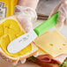 A person using a Choice stainless steel sandwich spreader with a neon green handle to make a sandwich.