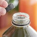 A hand pouring liquid into a black juice bottle with a tamper-evident cap on a counter.