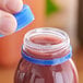 A hand holding a blue unlined tamper-evident cap over a jar of liquid.