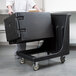 A man pushing a black Cambro dolly with a large black container on wheels.