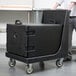 A man using a Cambro Camdolly to transport a black Cambro tray carrier.