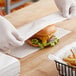 A person in gloves putting a cheeseburger in a Choice dry wax paper wrapper.