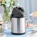 An Acopa stainless steel and black airpot on a table with a cup of coffee.
