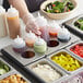 A person holding a Choice squeeze bottle pouring sauce into a tray of food with condiments.