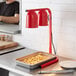 A man using an Avantco red free standing heat lamp to warm a tray of french fries on a counter.