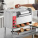 A woman using an Avantco vertical conveyor bun toaster to toast bread in a professional kitchen.