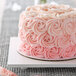 A cake with pink frosting on a white square cake board with feet.