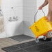 A person using a yellow bucket to fill a Regency stainless steel mop sink.