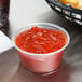 A Dart plastic container of ketchup next to a basket of fries.