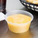 A Dart clear plastic souffle cup filled with yellow liquid on a table with a basket of food.