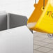 A yellow bucket of soapy water being poured into a Regency corner mop sink.