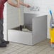 A man cleaning a Regency stainless steel mop sink with a mop.