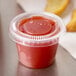 A Dart Conex clear plastic souffle cup filled with red sauce on a table.