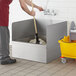 A man using a mop to clean a Regency stainless steel three-sided splash for a mop sink.