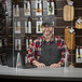 A man in a hat and apron behind a clear acrylic countertop safety shield.