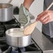 A person cooking food in a Choice aluminum sauce pan on a stove.