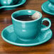 A turquoise Fiesta saucer with a tea cup and tea bag on it.