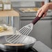 A hand using a Mercer Culinary Hell's Handle fish/egg turner to stir food in a pan.