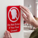 A person holding a red and white Tablecraft plastic sign with a head and text reading "Do Not Enter If You Feel Unwell"