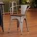 A Lancaster Table & Seating metal arm chair with a walnut wood seat on a wood floor.