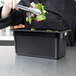 A chef using black Cambro food pan tongs to serve salad at a salad bar.