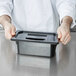 A person holding a black rectangular plastic container with a black Cambro lid.