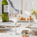 A white Acopa Radiance wine glass with a gold rim on a table with a glass of white wine.