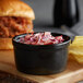 A bowl of pulled pork with a side of coleslaw on a table with chips and a burger.