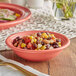 A coral Acopa Capri stoneware fruit bowl filled with food on a table.