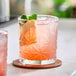 A pink beverage with ice, a citrus slice, and mint leaves served in an 11 oz. Acopa Gardenia rocks glass.