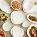 A table with Acopa Nova cream white stoneware plates and bowls on it.