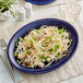 An Acopa Capri Deep Sea Cobalt oval stoneware coupe platter with a plate of food and a fork on a table.