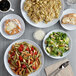 A table with Acopa Lunar white coupe plates of food, including pasta, salad, and a pastry with white frosting.