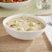 An Acopa Nova cream white stoneware bowl filled with soup on a table.